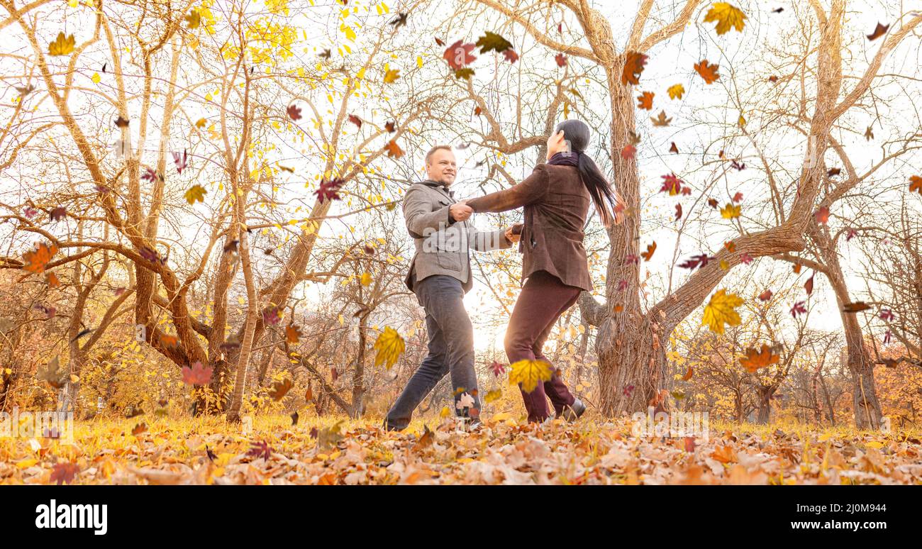 Ein Mann und eine Frau, die sich zusammenwirbeln Hände halten und sonniges Herbstwetter im Park genießen. Zwei Liebende schauen sich in an Stockfoto