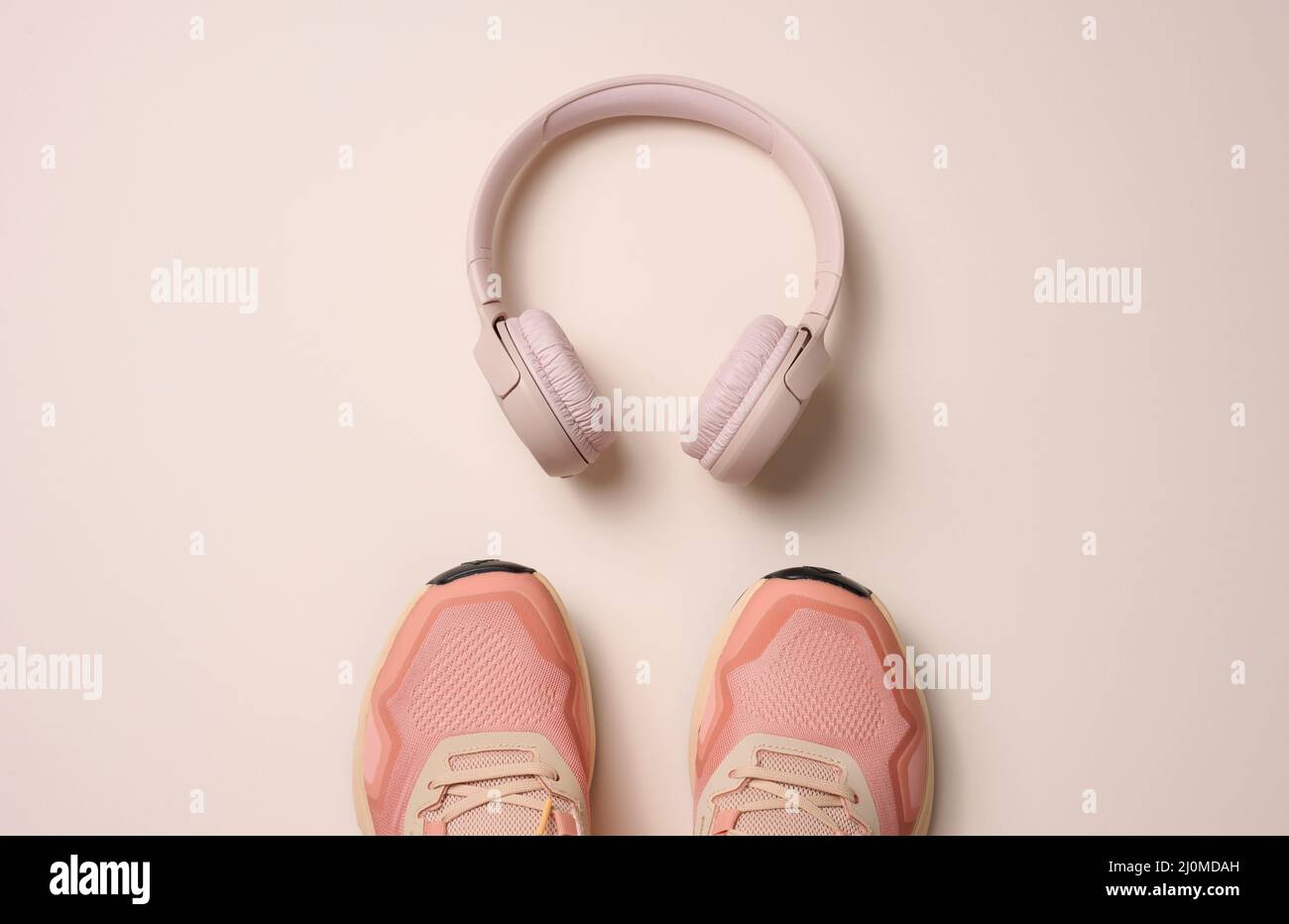 Ein Paar rosa Textil-Sneakers, kabellose Kopfhörer auf beigem Hintergrund. Für den Sport geeignet Stockfoto