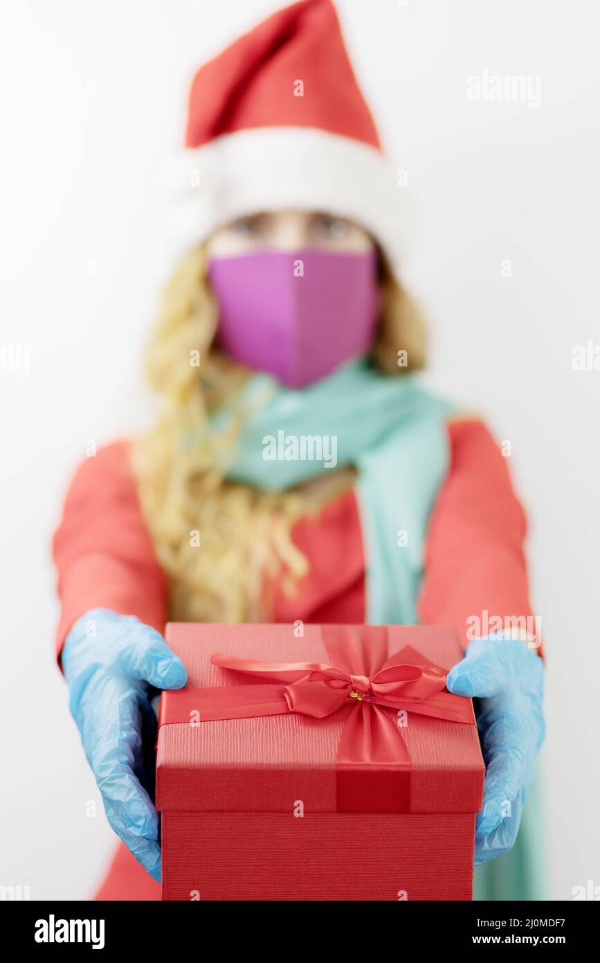 Santa Dame mit roter Geschenkbox. Medizinischer steriler Schutz für Weihnachten. Fokus auf den Vordergrund Stockfoto