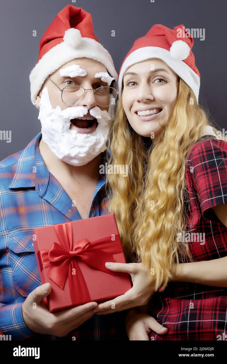 Der weihnachtsmann und die Weihnachtsfrau sitzen zusammen und halten eine rote Geschenkbox mit einer Schleife. Ein Geschenk für zwei Personen Stockfoto
