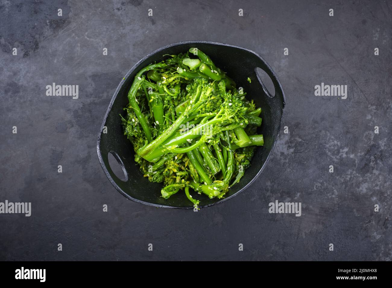 Frischer Rapini-Brokkoli-rabe mit Sesam als Draufsicht auf einer schwarzen Schüssel mit Kopierraum Stockfoto