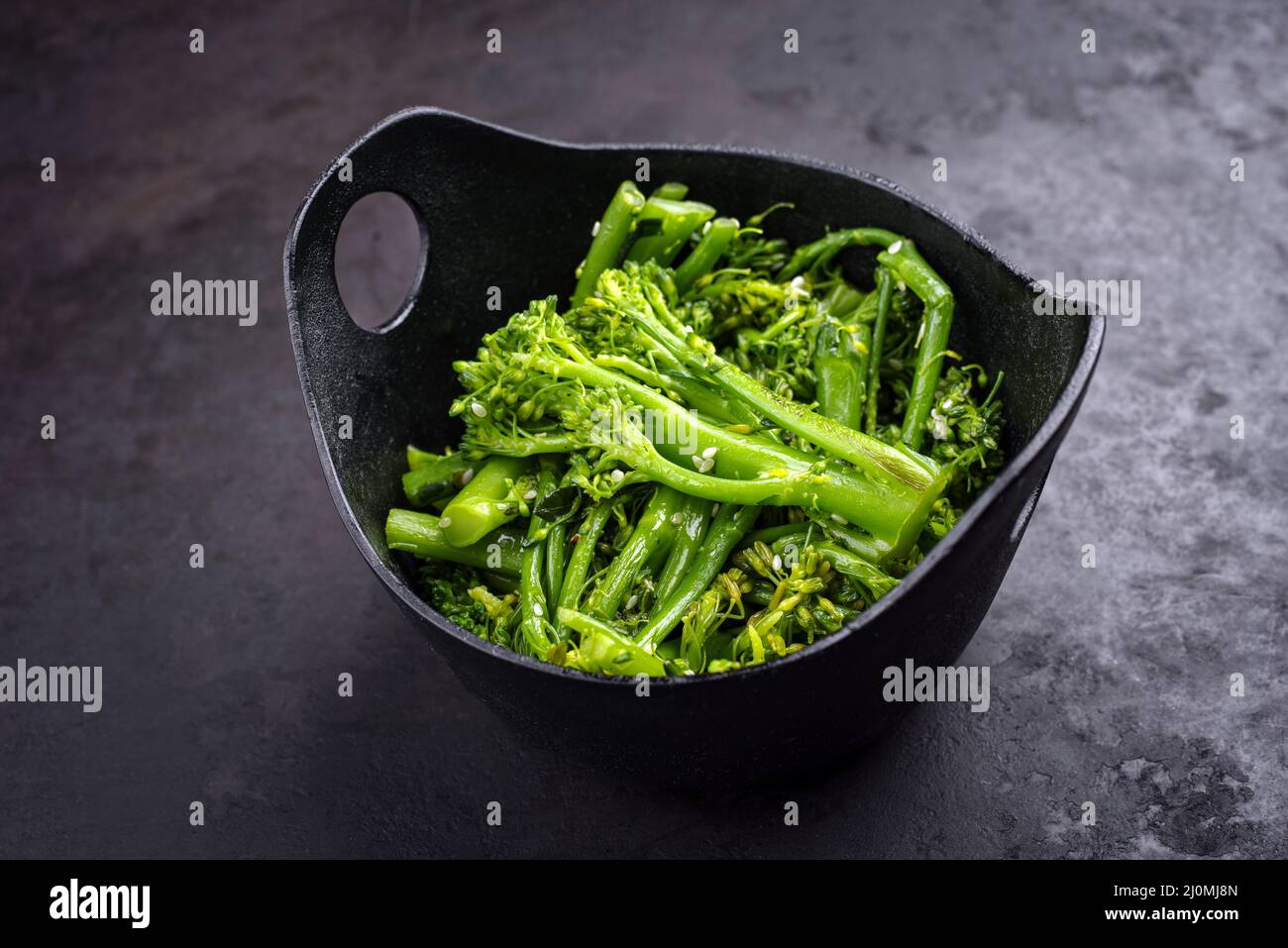 Frischer Rapini-Brokkoli-rabe mit Sesam als Draufsicht auf einer schwarzen Schüssel mit Kopierraum Stockfoto