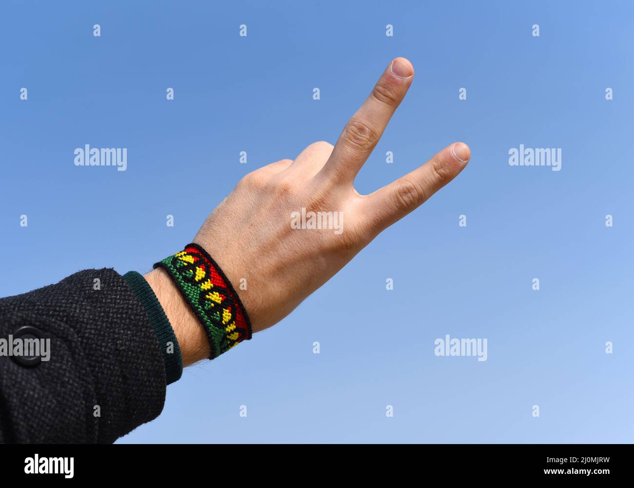 Handgemachtes DIY Freundschaftsarmband mit Rasta-Flaggenmuster mit einem Friedenssymbol am männlichen Handgelenk auf Himmelshintergrund. Stockfoto