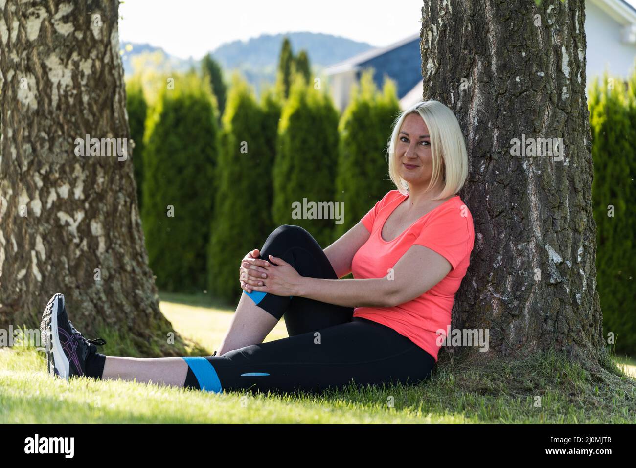 Junge attraktive Sportlerin lächelt, während sie sich unter Bäumen entspannt Stockfoto