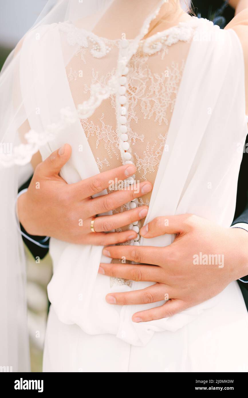 Die Hände des Bräutigams umarmen die Taille der Braut in einem weißen Spitzenkleid. Nahaufnahme. Rückansicht Stockfoto