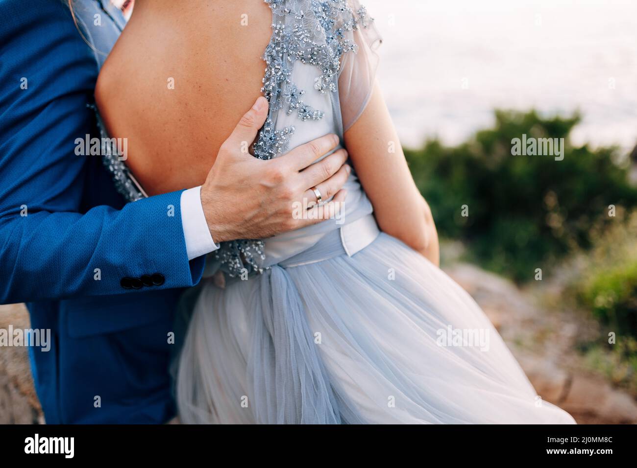 Der Bräutigam legte seine Hand auf den Rücken der Braut, während er am Strand in der Nähe des Meeres stand. Nahaufnahme Stockfoto