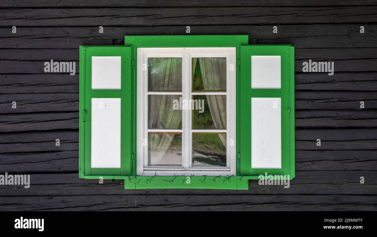 Altes antikes weißes Vintage-Holzfenster mit grünem Umriss und Fensterläden an der braunen Holzwand. Stockfoto
