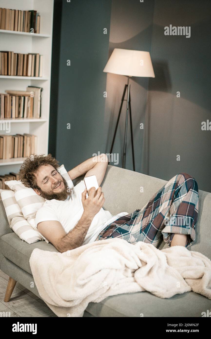 Lächelnder 20 Jahre alter Mann im Chat mit seinem Freund von Video Mobile Messenger. Big Boy vor dem Schlafen Gespräche mit seiner Mutter. Home De Stockfoto