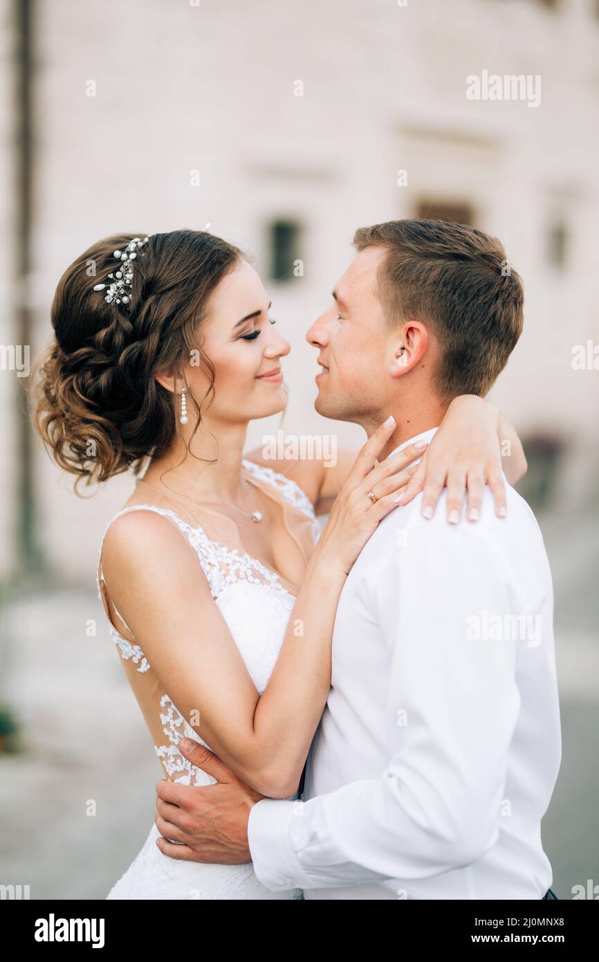 Kotor, Montenegro - 20.06.17: Lächelnde Braut in einem weißen Spitzenkleid umarmt sich am Hals. Der Bräutigam umarmt die Taille der Braut. Nahaufnahme Stockfoto