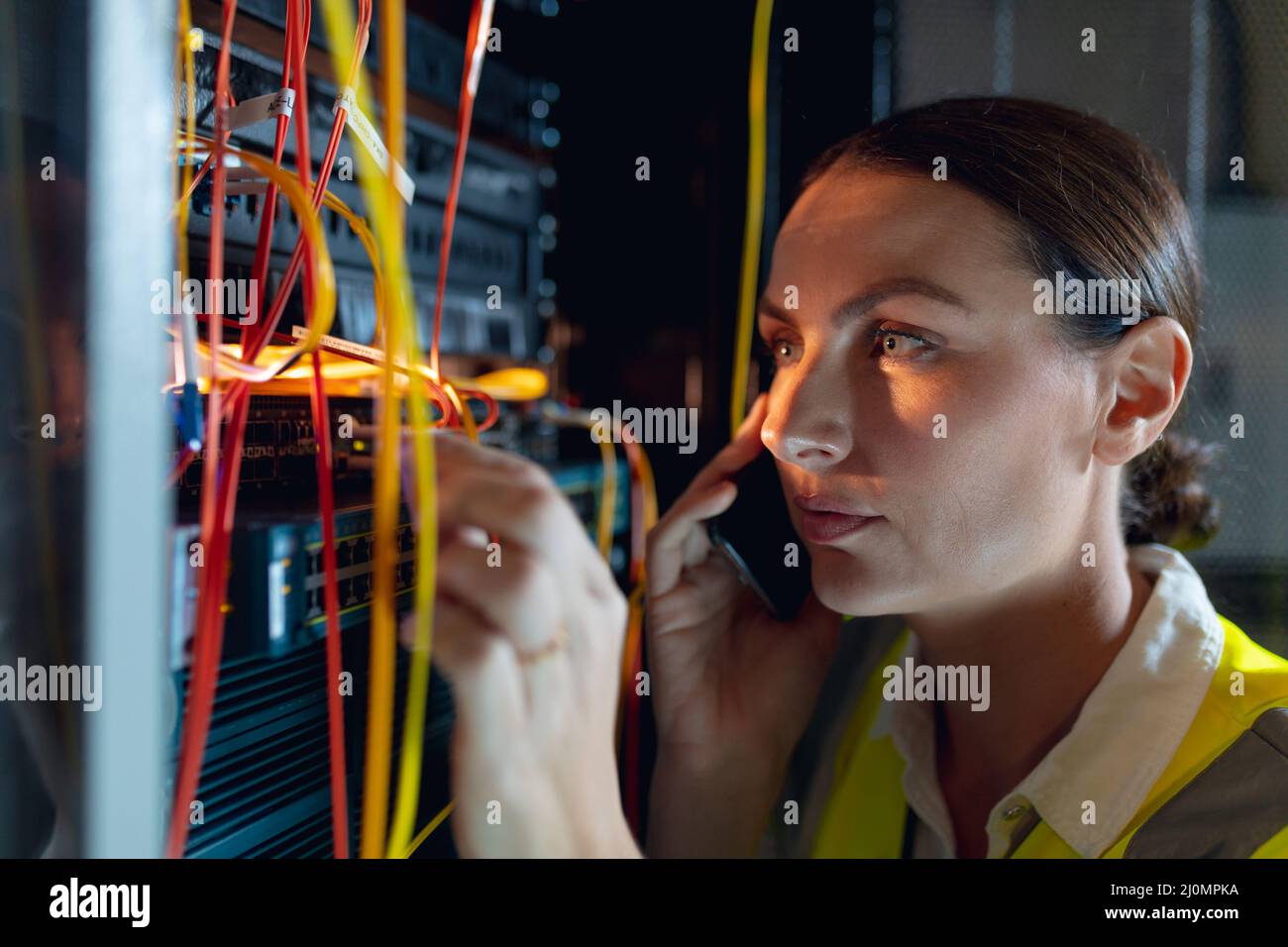 Nahaufnahme einer kaukasischen Ingenieurin, die auf dem Smartphone spricht, während sie im Computerserverraum inspiziert Stockfoto