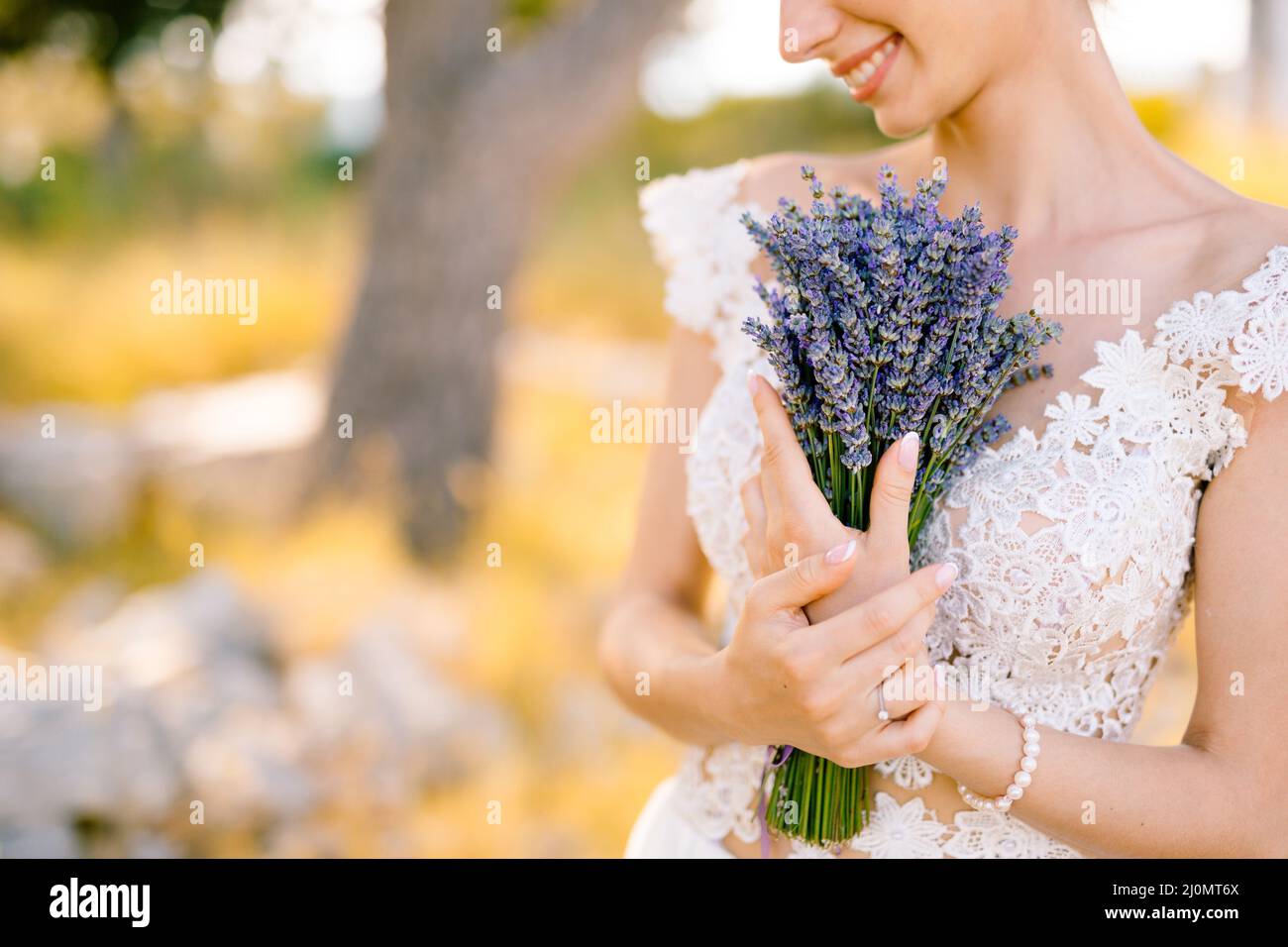 Sibenik, Kroatien - 05.06.17: Lächelnde Braut mit einem Ring und einem Perlenarmband auf der Hand in einem weißen Spitzenkleid drückt einen Strauß Stockfoto