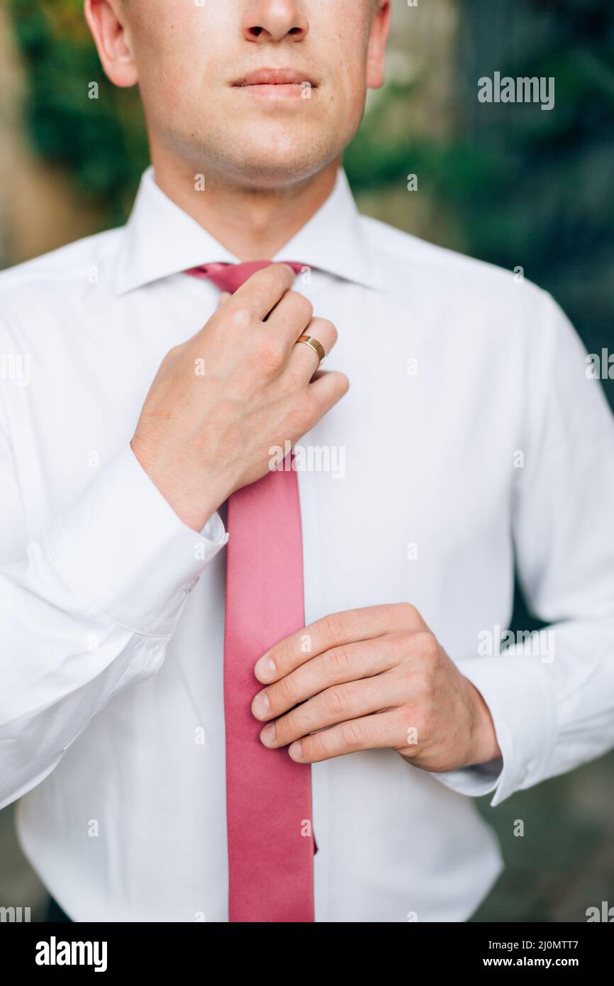 Kotor, Montenegro - 20.06.17: Bräutigam in einem weißen Hemd strafft seine rosa Krawatte. Nahaufnahme Stockfoto