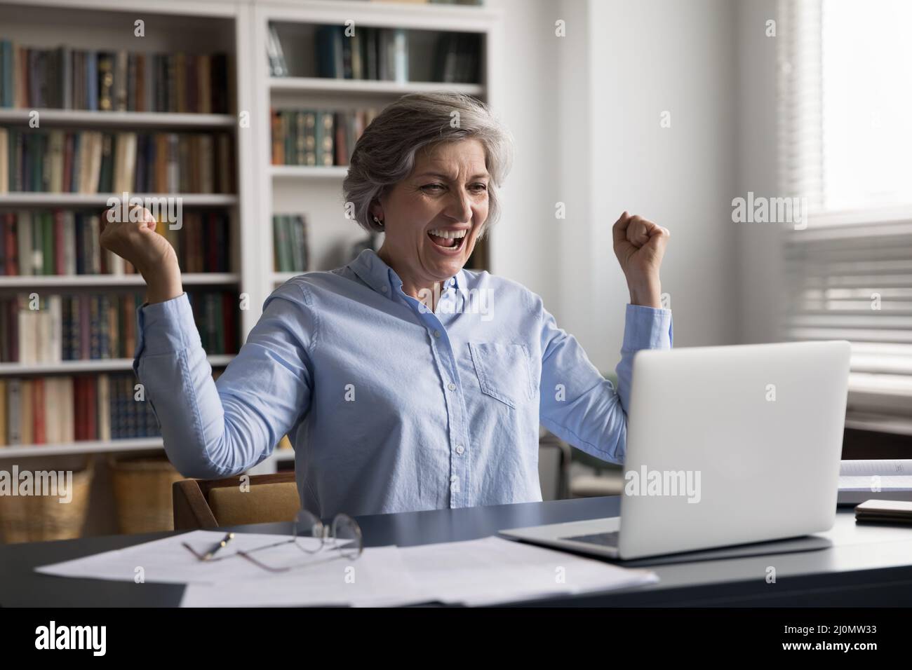 Eine glückliche ältere Geschäftsfrau freut sich, wenn sie gute Nachrichten auf einem Laptop liest Stockfoto