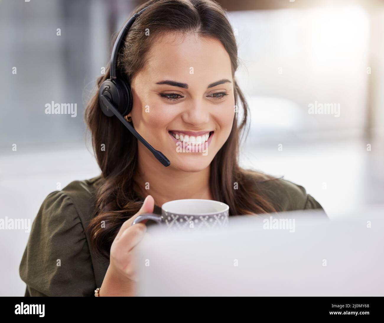 Einen weiteren erfolgreichen Tag durchstehen. Aufnahme eines jungen Callcenter-Agenten, der Kaffee trinkt, während er an einem Computer in einem Büro arbeitet. Stockfoto