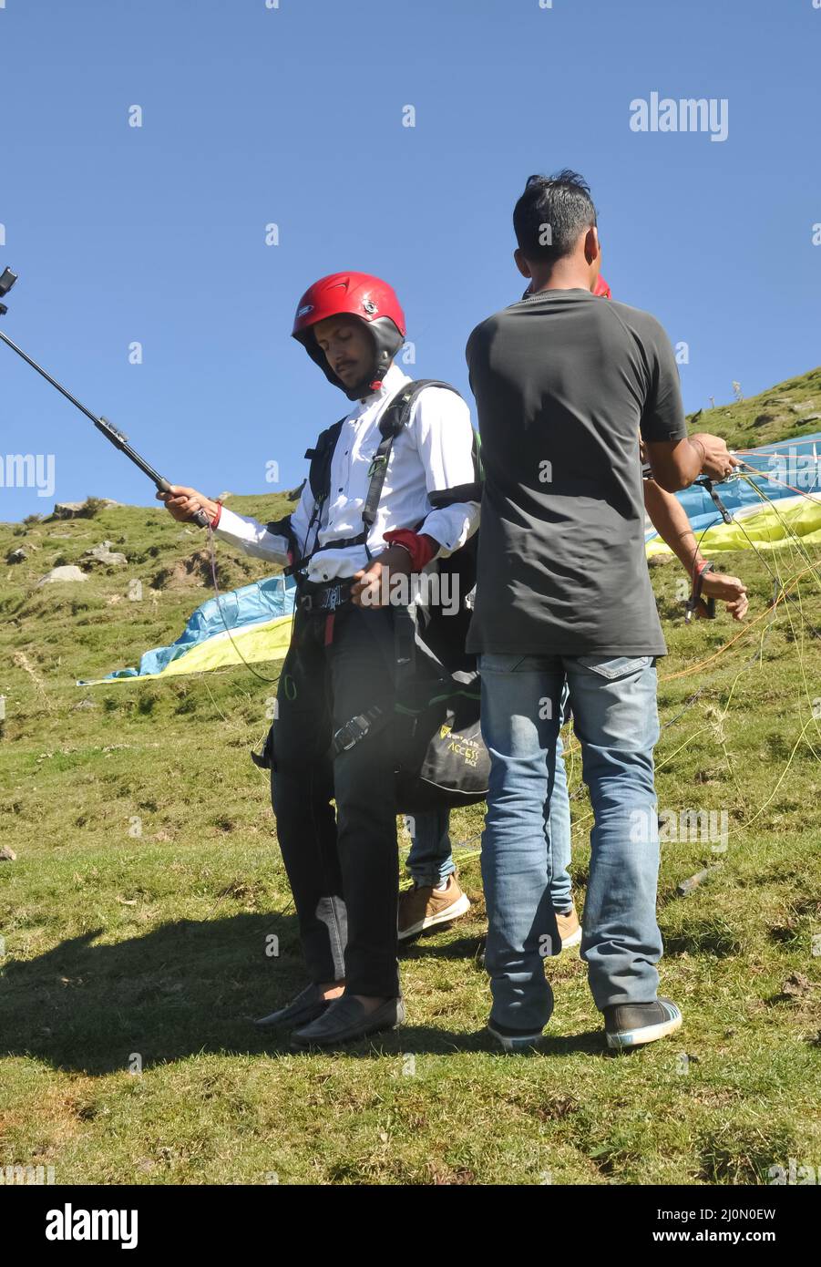 Mandi, Himachal Pradesh, Indien - 10 16 2021: Ein männlicher Tourist, der mit GoPro ein Video für Erinnerungen macht, während ihm Gleitschirmflieger dabei helfen, den Fallschirm im Berg zu justieren. Stockfoto