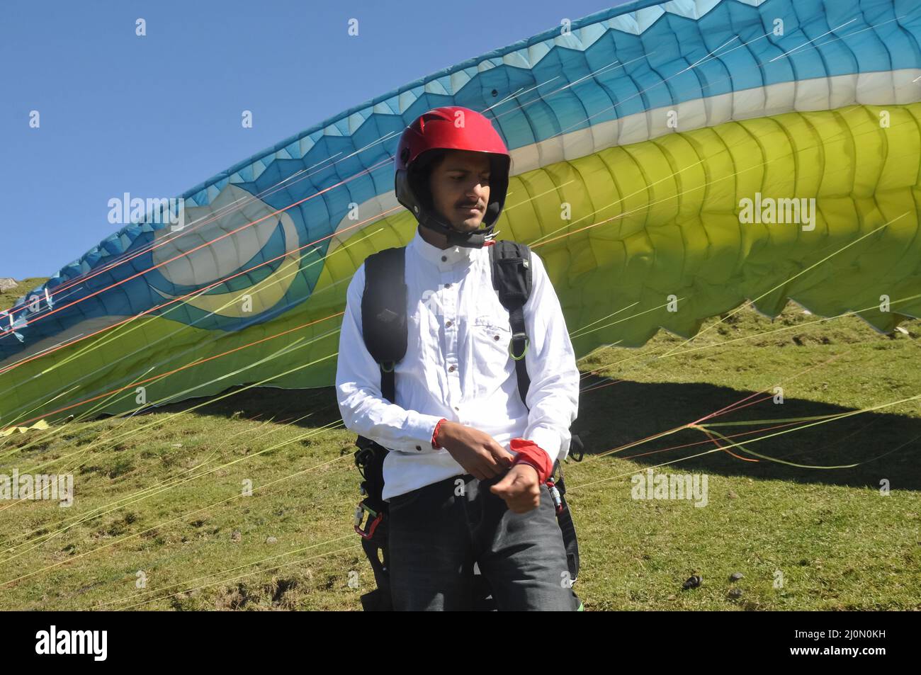 Ein nordindischer junger Mann, der während der Vorbereitung des Gleitschirmfluges seitwärts schaut. Stockfoto