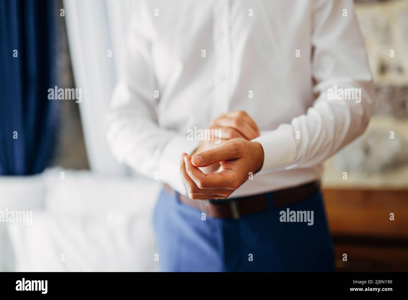 Mann in blauer Hose knöpft einen Knopf an der Manschette eines weißen Hemdes. Nahaufnahme Stockfoto
