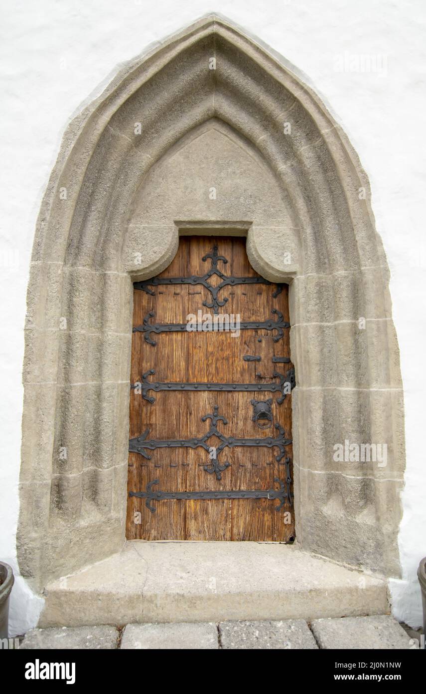 Gewölbte antike Kirche Holztür mit schwarzen Eisenornamenten in einer Steinwand. Stockfoto