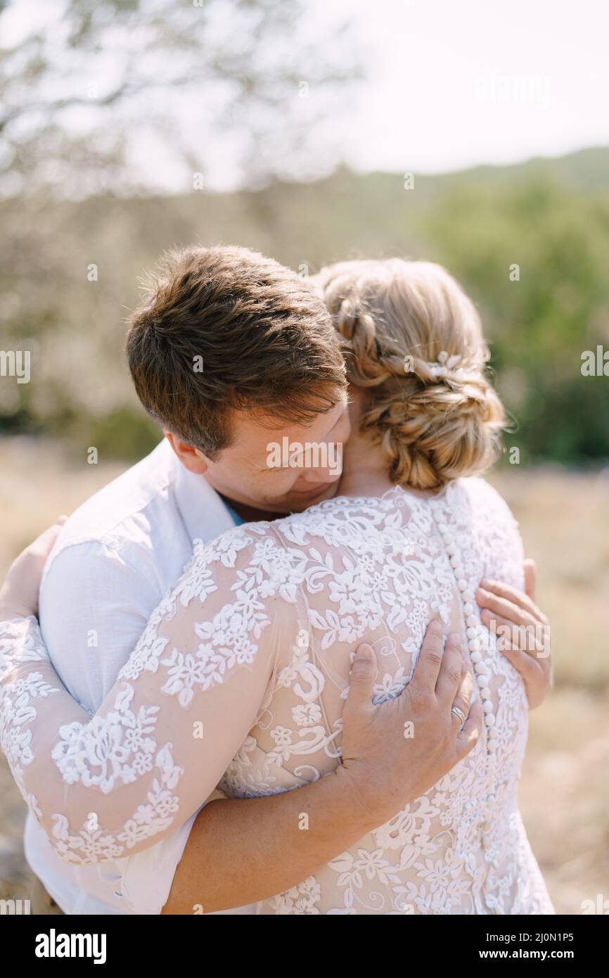 Braut und Bräutigam umarmen sich auf dem Hintergrund von Bäumen. Nahaufnahme Stockfoto