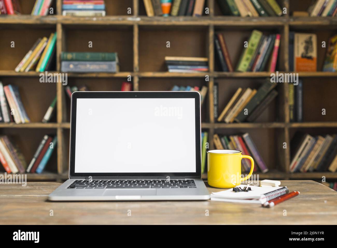 Kaffeetasse, Laptop mit Schreibwaren, Holzschreibtisch, Bibliothek Stockfoto