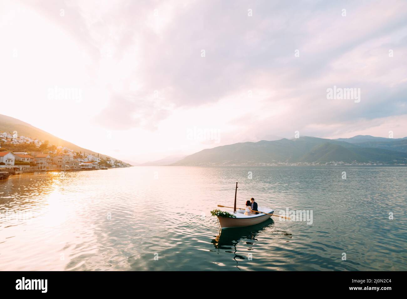 Mann rollt Frau in einem Boot mit Blumen auf dem Wasser auf den Bergen und Sonnenuntergang Stockfoto