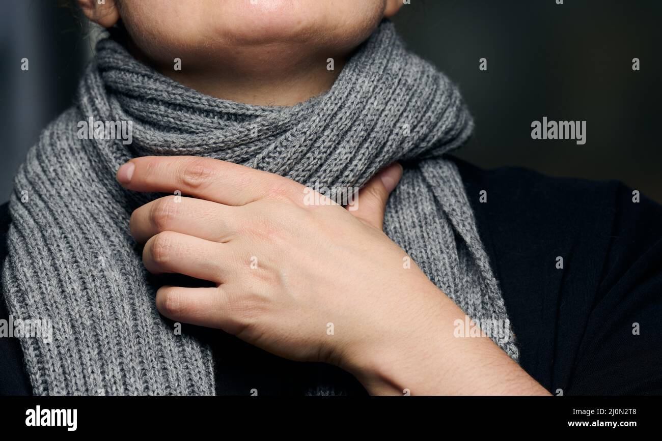 Ein grauer Schal ist um den Hals gewickelt, und eine Hand hält den Hals.  Erkältung und Halsschmerzen Stockfotografie - Alamy