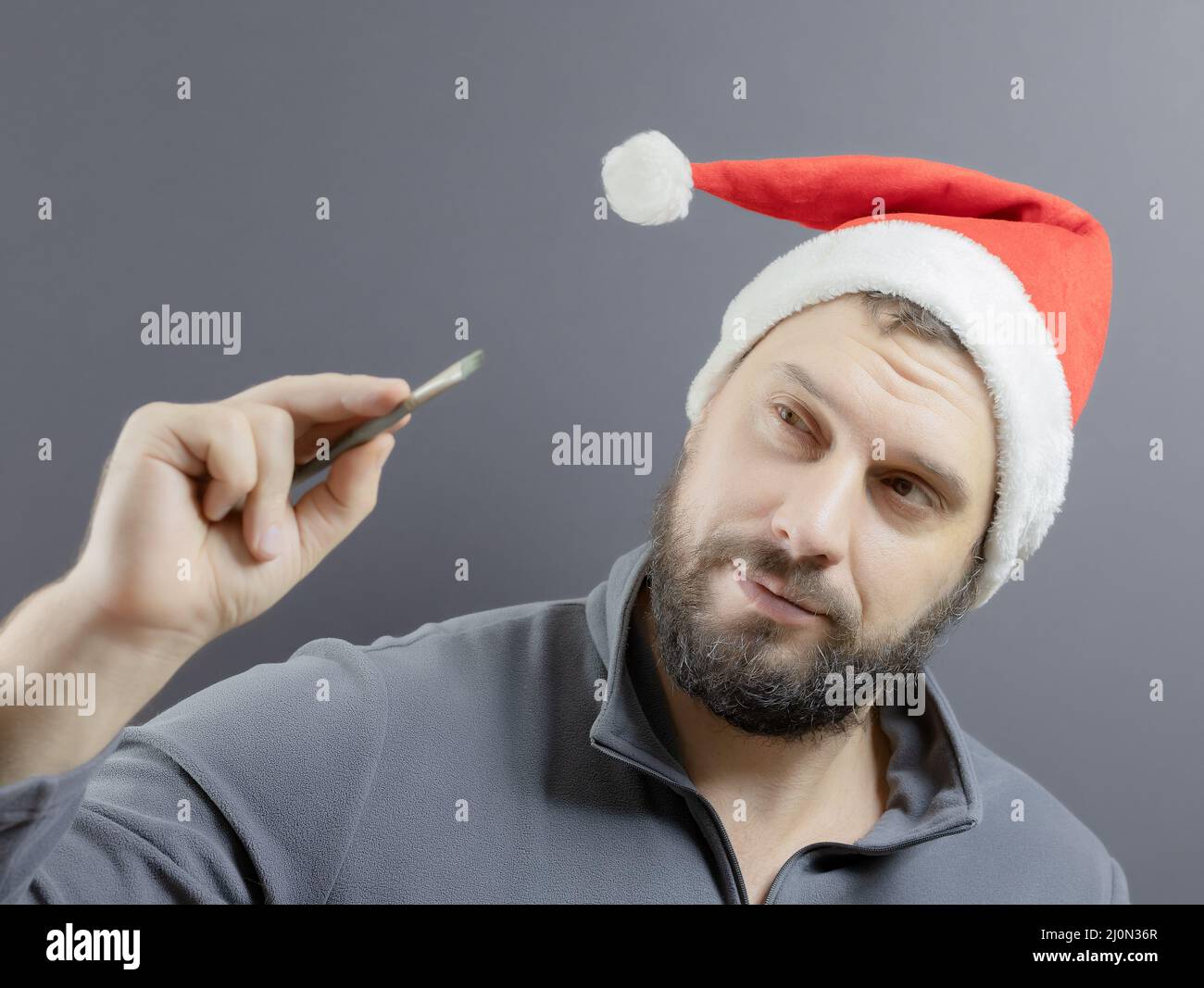 Ein bärtiger Mann in einem roten weihnachtsmann-Hut hält einen Kunstpinsel in der Hand. Santa-Künstler. Weichfokus Stockfoto