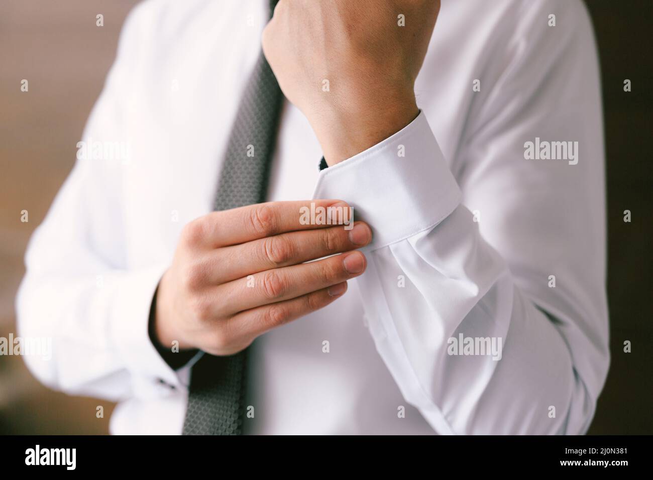 Mann in einer Krawatte knöpft die Ärmel eines weißen Hemdes hoch. Nahaufnahme Stockfoto