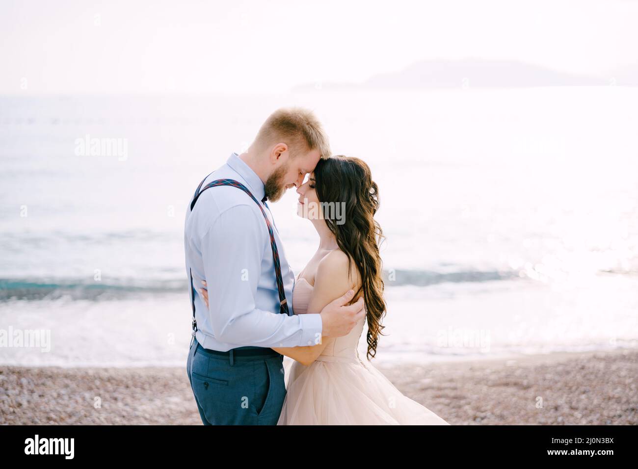 Die Braut und der Bräutigam stehen auf dem Kiesstrand und umarmen sich Stockfoto