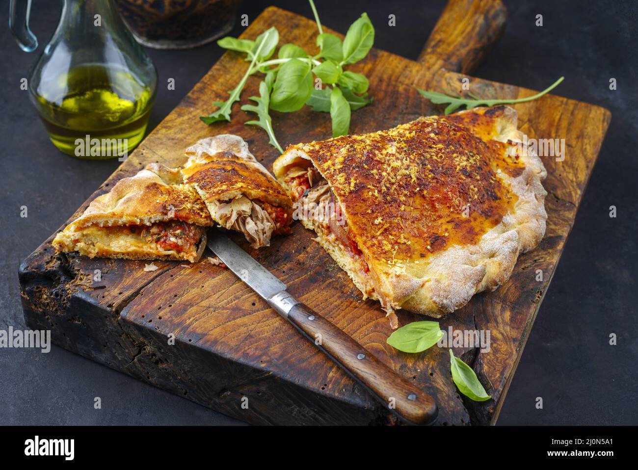 Traditionelle italienische Pizza Calzone mit Thunfisch und Zwiebeln, die als Nahaufnahme auf einem rustikalen alten Holzbrett serviert werden Stockfoto