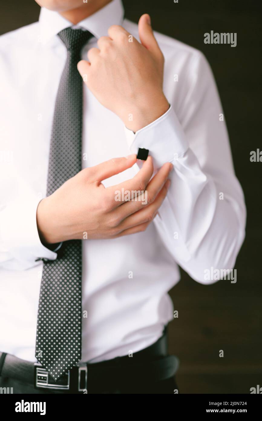 Mann in einer Krawatte und Hose knöpfte einen Manschettenknöpfe auf dem Ärmel eines weißen Hemdes Stockfoto