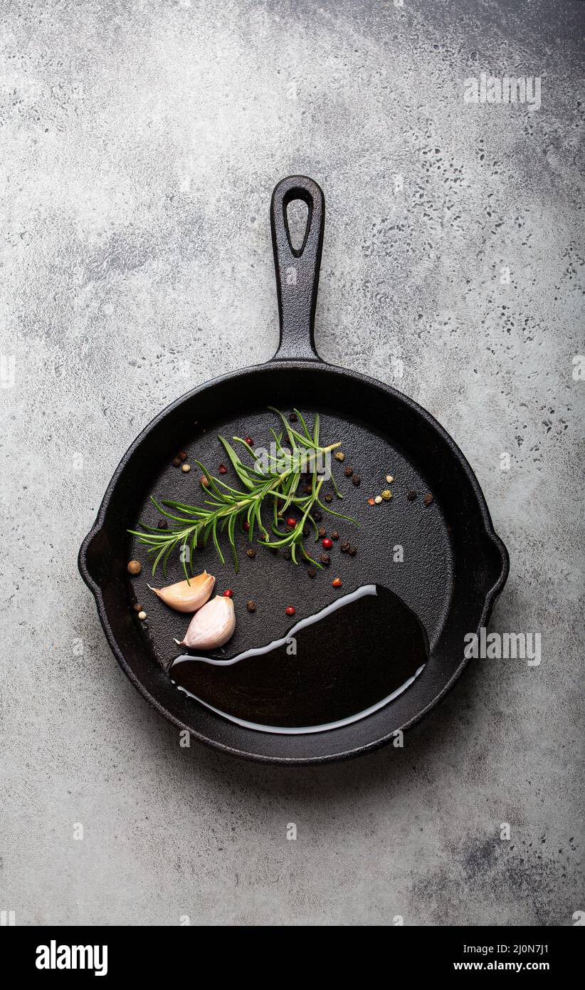 Schwarze gusseiserne Bratpfanne mit Rosmarin, Knoblauch, Pfeffer, Öl Stockfoto