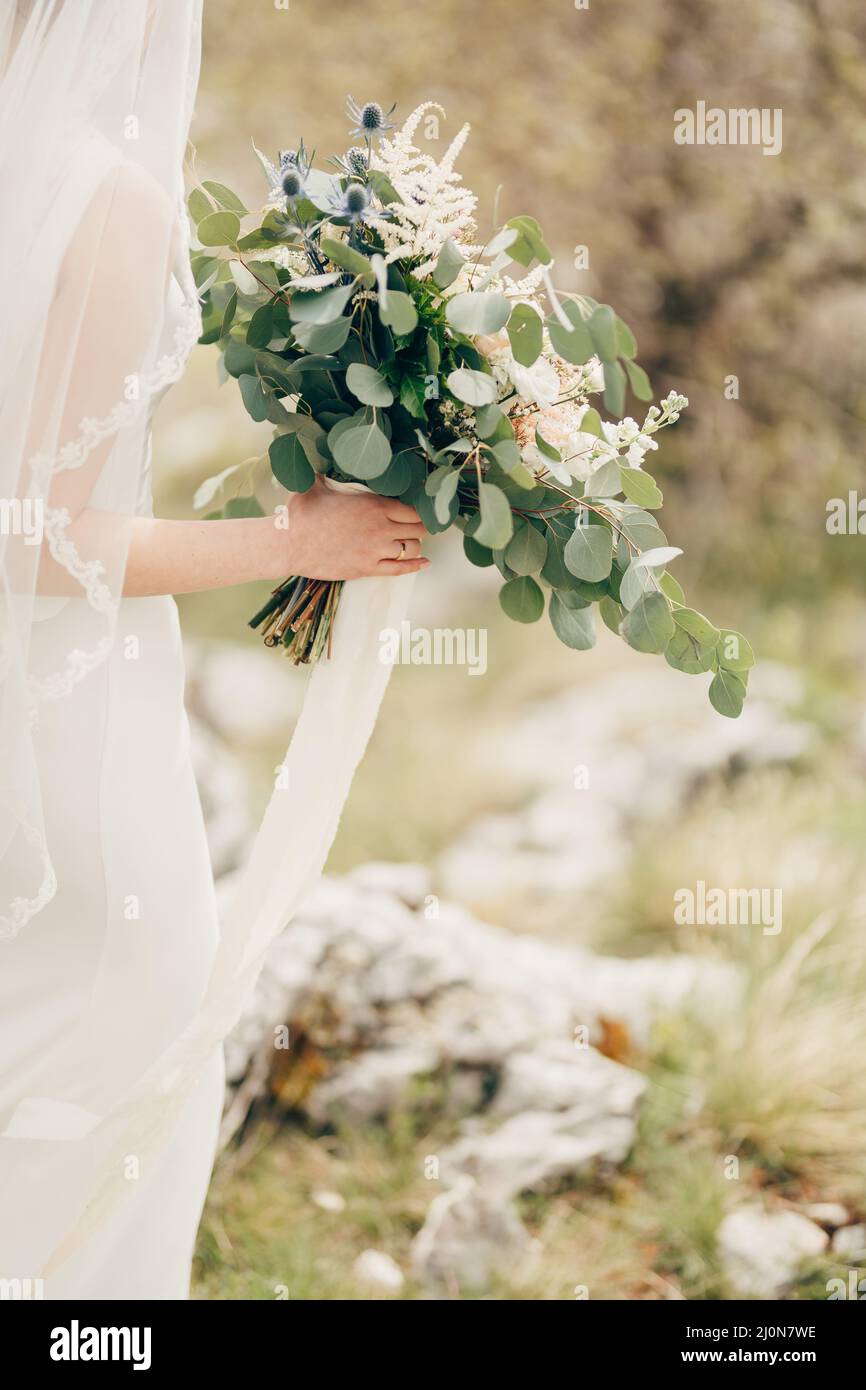 Blumenstrauß in den Händen der Braut in einem weißen Kleid mit Schleier. Nahaufnahme Stockfoto