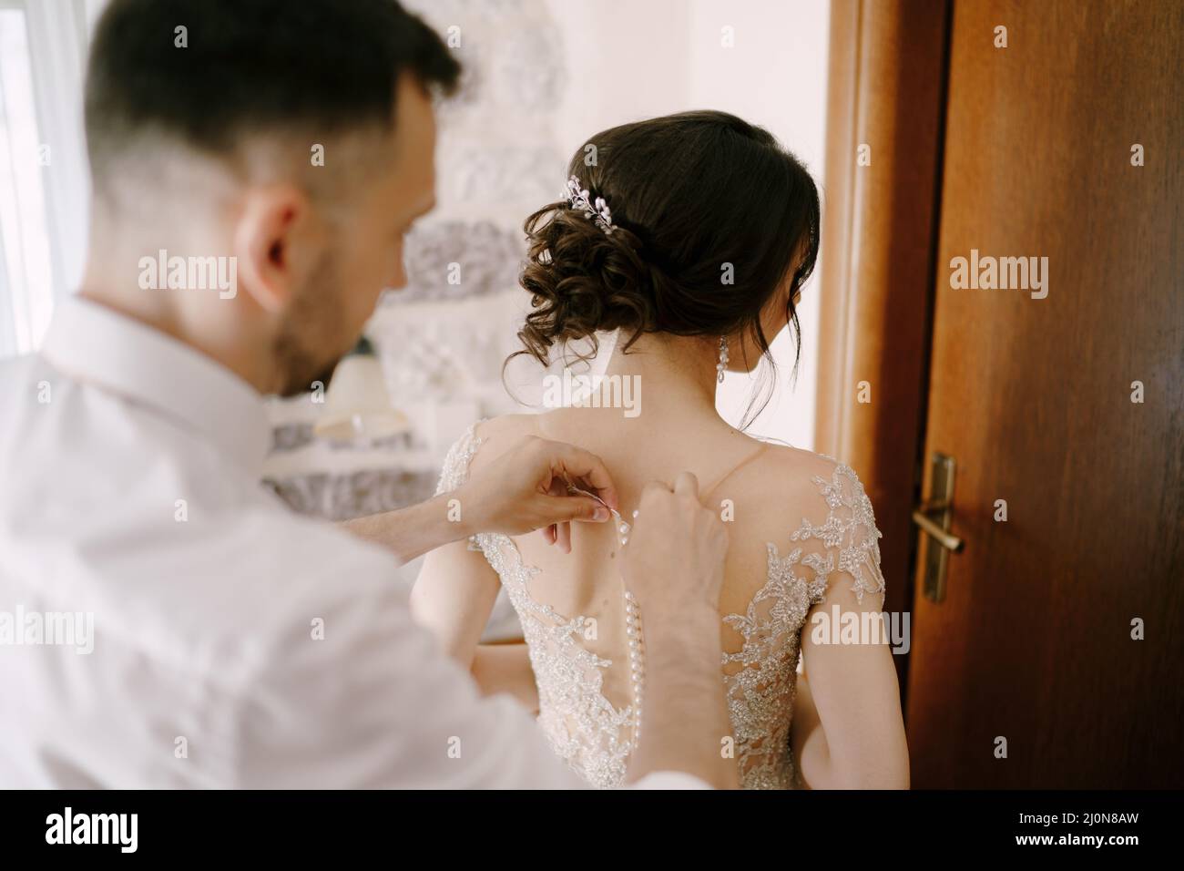 Der Bräutigam schließt die Knöpfe am Brautkleid. Nahaufnahme Stockfoto