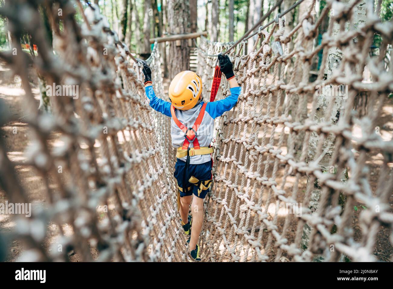 Boy geht über eine Gitterbrücke und hält sich an einem Kabel fest. Rückansicht Stockfoto