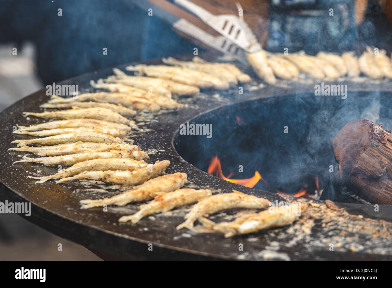 Das Zubereiten von traditionellem, schmackhaftem gebratenem europäischem Fisch, der auf einem Straßenmarkt am offenen Feuer gekocht wird, verzehrfertig, Street Food in Vilnius Stockfoto