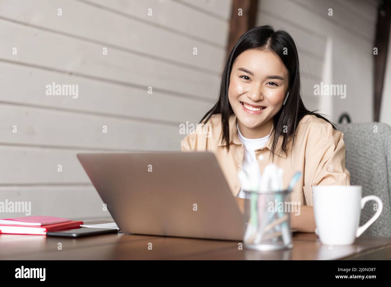 Lächelndes koreanisches Mädchen arbeitet von zu Hause aus, freiberufliche Mitarbeiterin arbeitet am Laptop, studiert oder macht Hausaufgaben am Computer Stockfoto