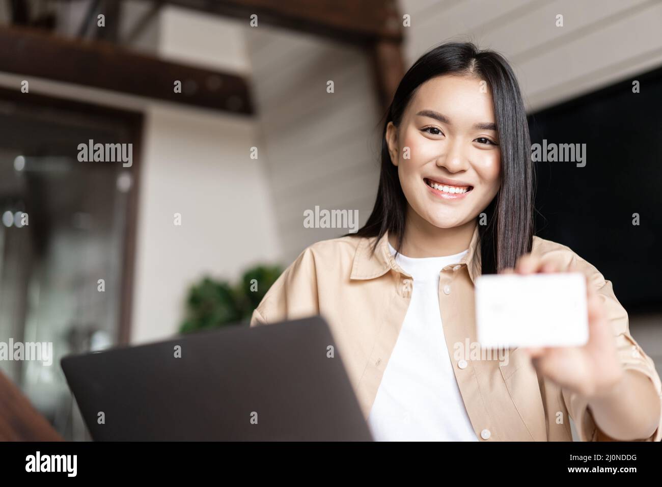 Online-Shopping. Junge Frau, die mit Kreditkarte bezahlt, über die Website auf dem Laptop kauft und zu Hause im Wohnzimmer sitzt Stockfoto