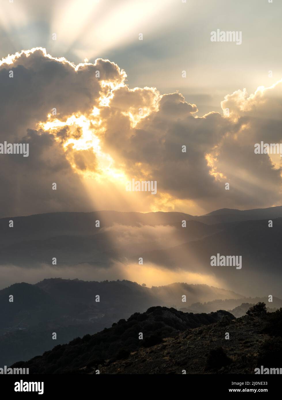 Helle Sonnenstrahlen leuchten bei Sonnenuntergang durch dunkle Wolken über dem Berg. Dramatischer Himmel im Winter Stockfoto