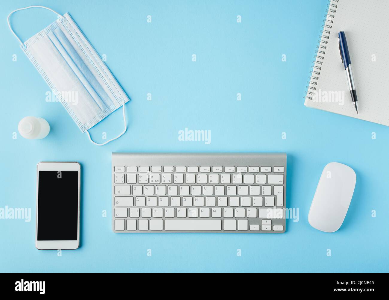 Moderner Schreibtisch in hellblauem Blau mit Medikamentenmaske und Desinfektionsmittel. Draufsicht. Soziale Distanz im Büro. Stockfoto