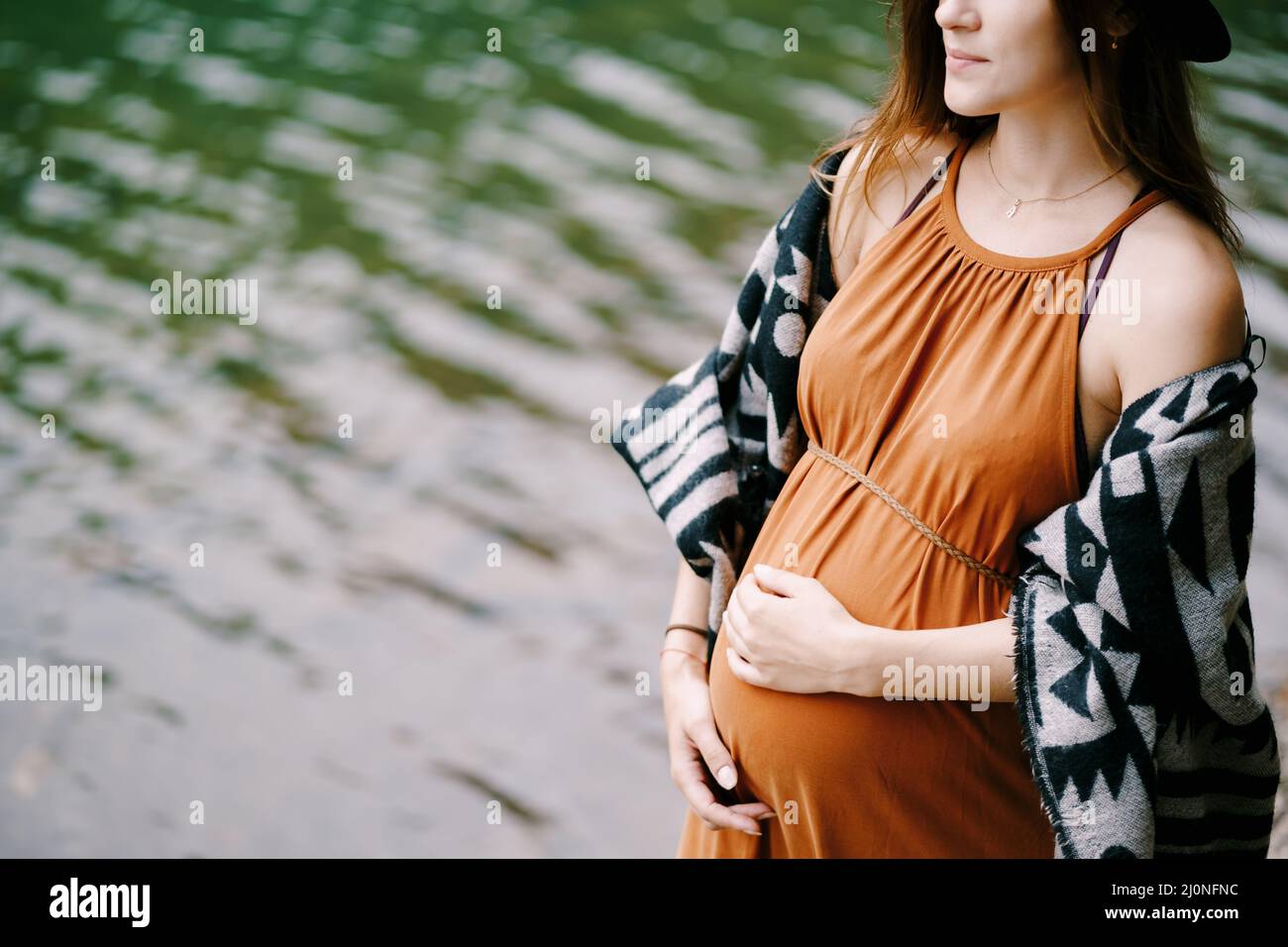 Eine Schwangere im Hut steht am See. Nahaufnahme Stockfoto