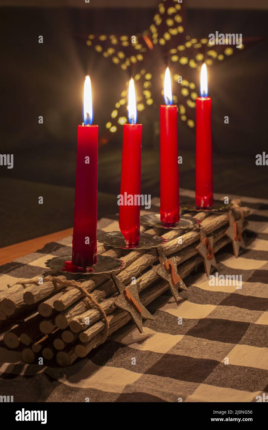 Advent Holzstäbchen Kerzenhalter mit silbernen Sternen mit den Nummern 1,2,3,4. Vier brennende rote Kerzen. Weihnachtsdekoration. Stockfoto