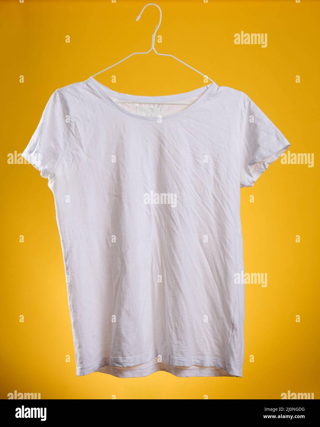 Weißes T-Shirt aus zerknitterter Baumwolle, das auf einem Kleiderbügel auf einem gelben Hintergrund hängt, Sommerkleidung Stockfoto