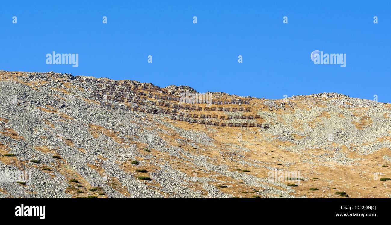 Lawinenschutz oder Barriere auf dem Lomnicke sedlo Bergpass in der Hohen Tatra mit Mond am blauen Himmel. Slowakei. Stockfoto