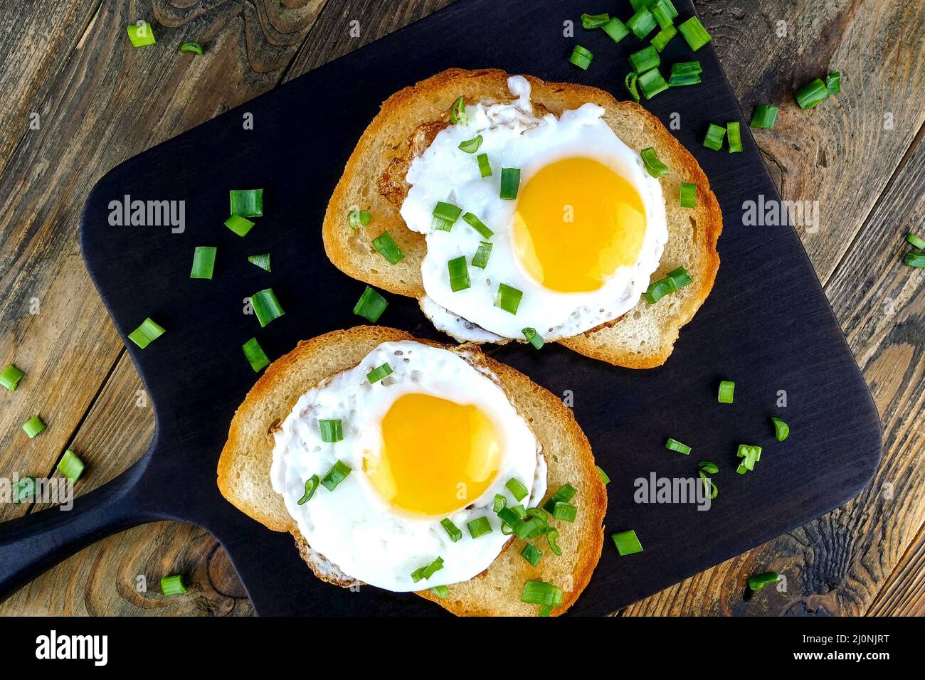Gebratenes Ei-Sandwich mit Eigelb, Chili auf gerösteter Brotscheibe, die mit grünen Zwiebeln bestreut ist. Selektiver Fokus. Draufsicht. Nahaufnahme. Stockfoto