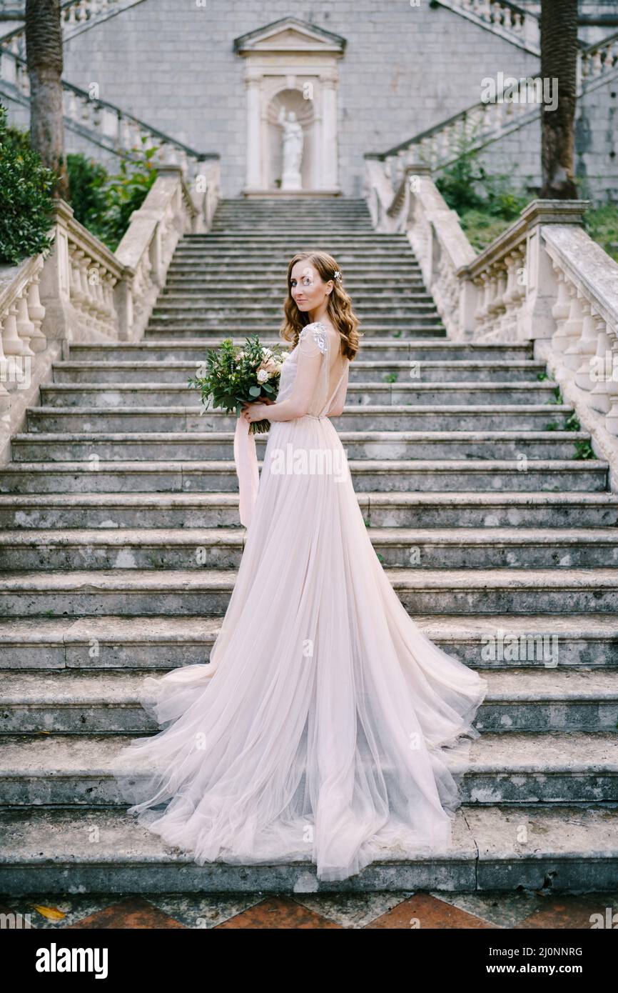 Braut in einem langen Kleid steht halb eingewickelt auf Steintreppen Stockfoto