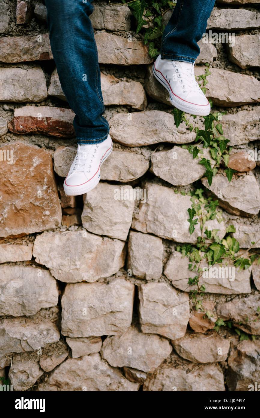 Männliche Beine in Jeans und Sneakers auf dem Hintergrund einer Steinwand im Park Stockfoto
