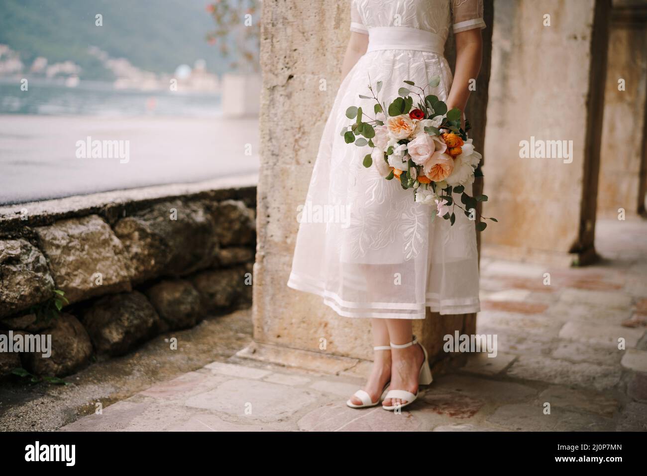 Braut mit Blumenstrauß steht in der Nähe einer Säule an der Küste. Nahaufnahme Stockfoto