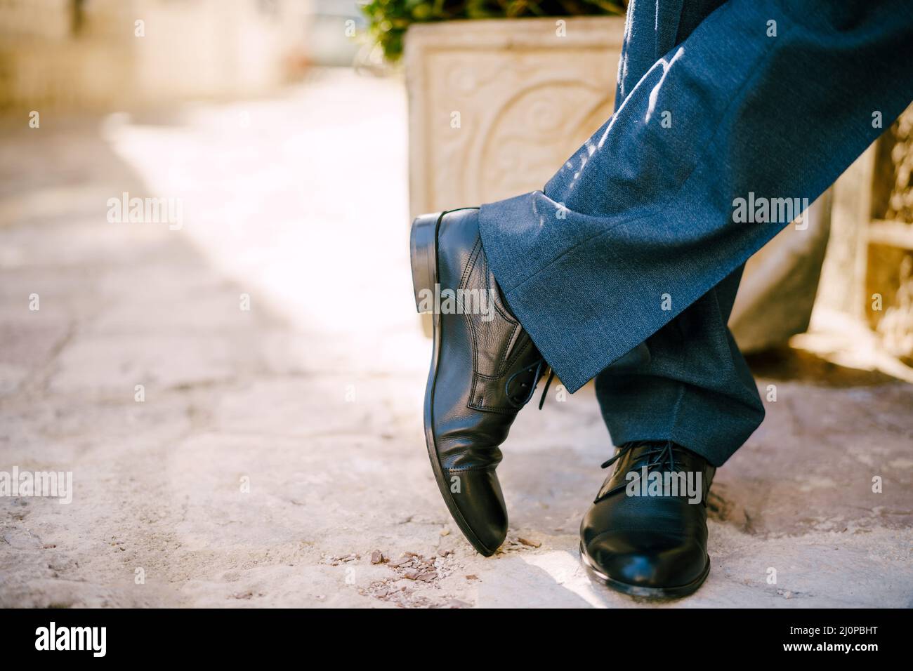 Männliche Füße in schwarzen Schuhen und blauen Hosen auf dem Steinboden. Nahaufnahme Stockfoto
