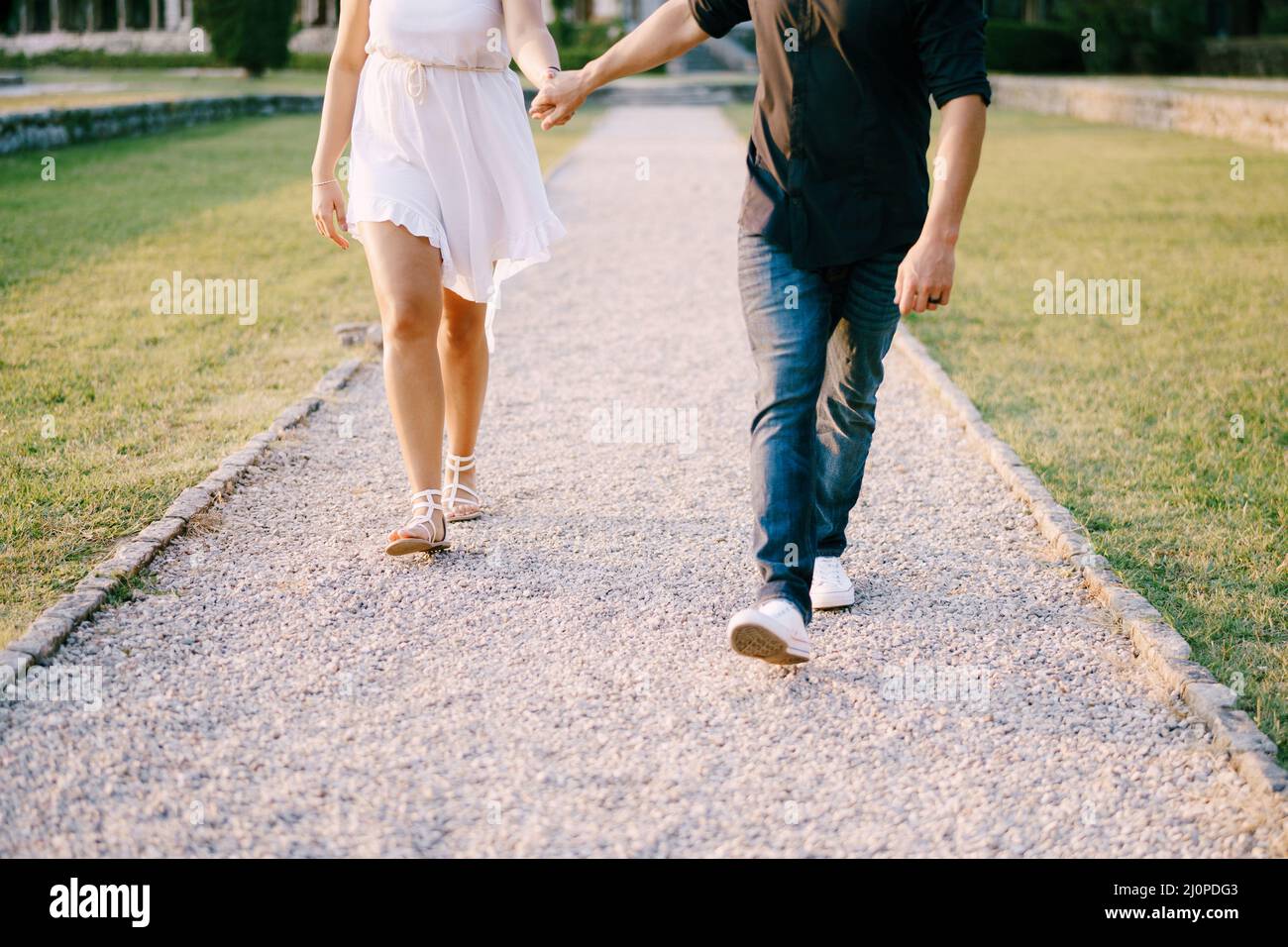 Mann und Frau, die den Schotterweg im Park entlang gehen, halten sich die Hände Stockfoto